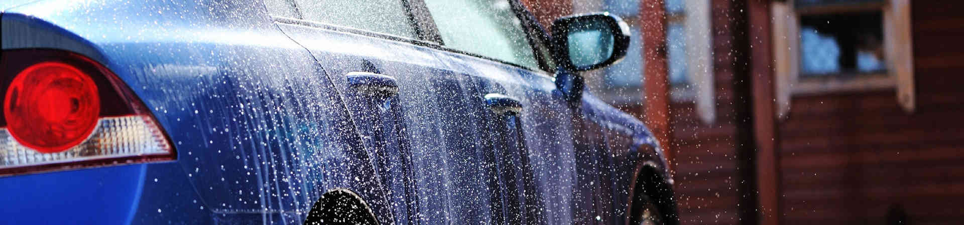 Cómo lavar el coche a mano paso a paso: el método de los dos cubos 2 Coche azul mojado durante el aclarado de la carrocería en el lavado a mano