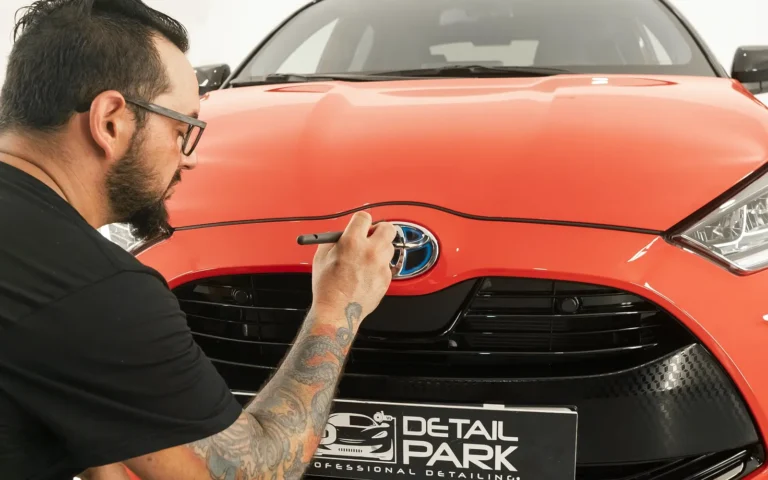 Alumno del curso de detailing limpiando con pincel el emblema de un Toyota Yaris rojo en Detail Park