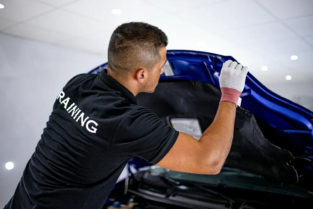Cursos de Paint Protection Film 8 Alumno del curso de PPF colocando la lámina bajo el capó de un coche azul
