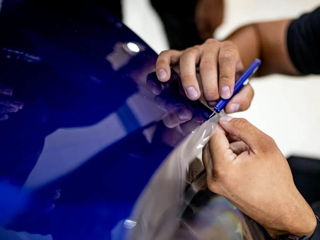Cursos de Paint Protection Film 12 Manos colocando lámina de PPF en el faro de un coche azul durante el curso de PPF