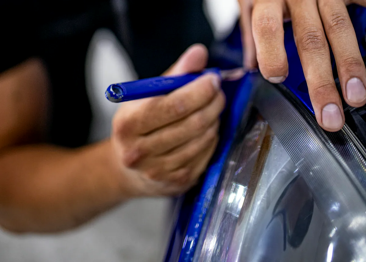 PPF coche: lo que debes saber antes de contratarlo 3 Rasqueta asentando la lámina de PPF en el faro de un coche azul en el taller de Detail Park
