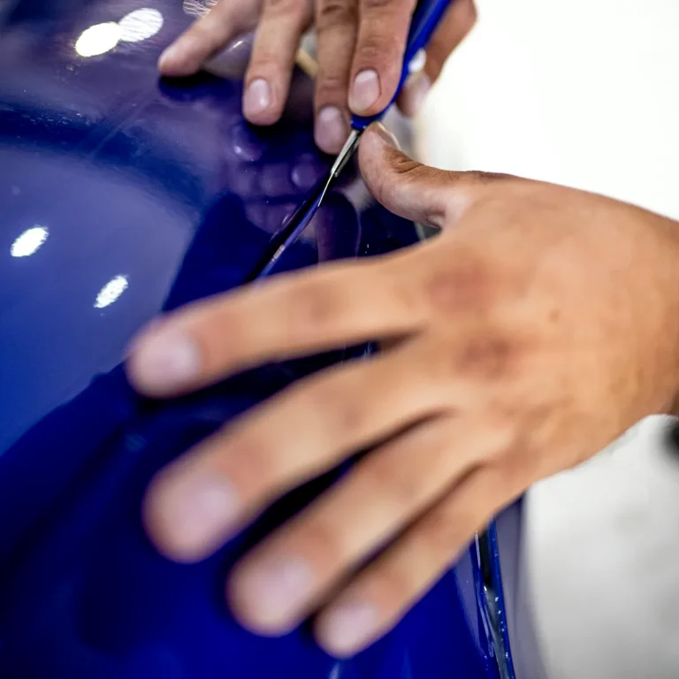 Cursos de Paint Protection Film 10 Manos tensando la lámina de PPF sobre la aleta de un coche azul con rasqueta