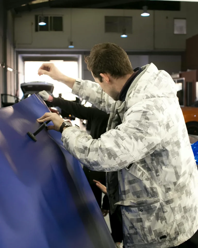 Alumno colocando vinilo azul en la puerta de un coche con rasqueta durante el curso de car wrapping