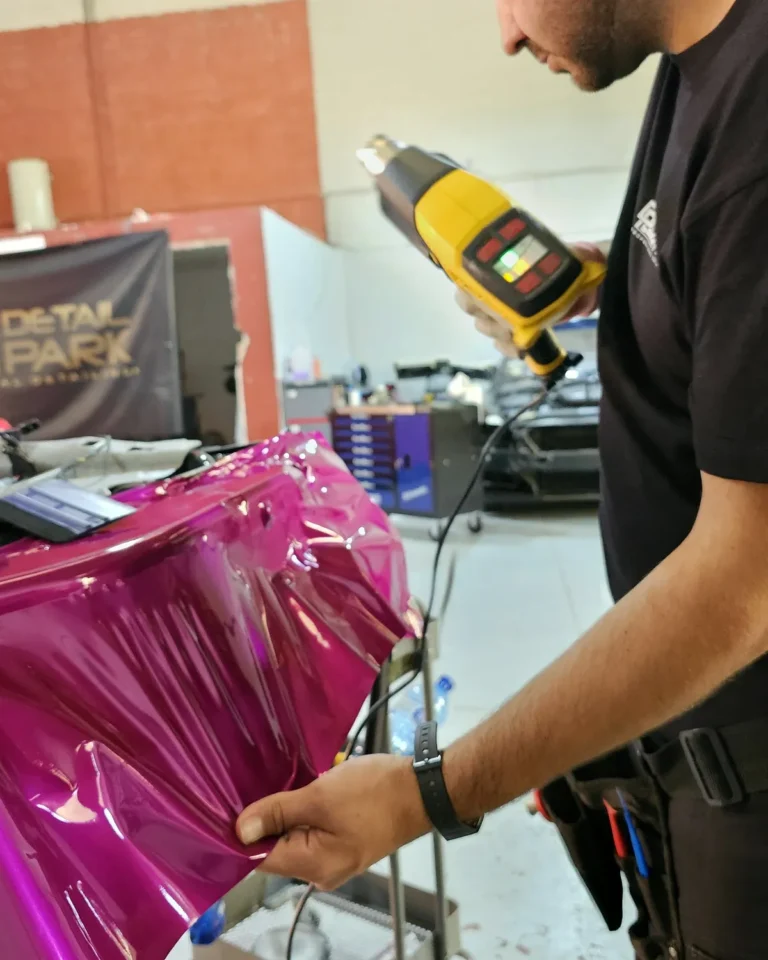 Alumno aplicando vinilo cromo magenta con pistola de calor en el curso de car wrapping