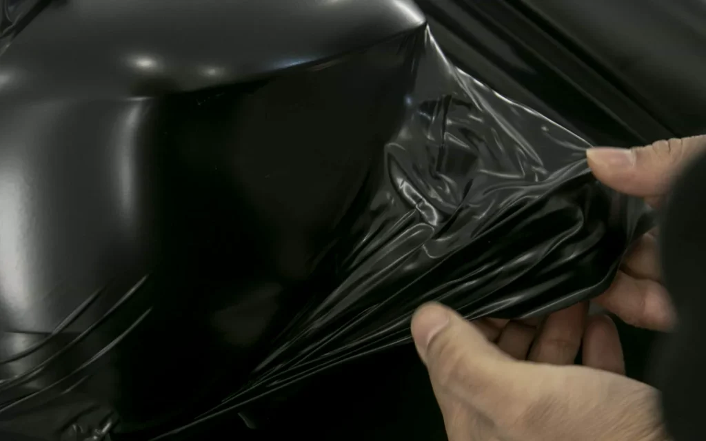 Curso de Car Wrapping 12 Manos estirando vinilo negro mate sobre un retrovisor en el curso de car wrapping