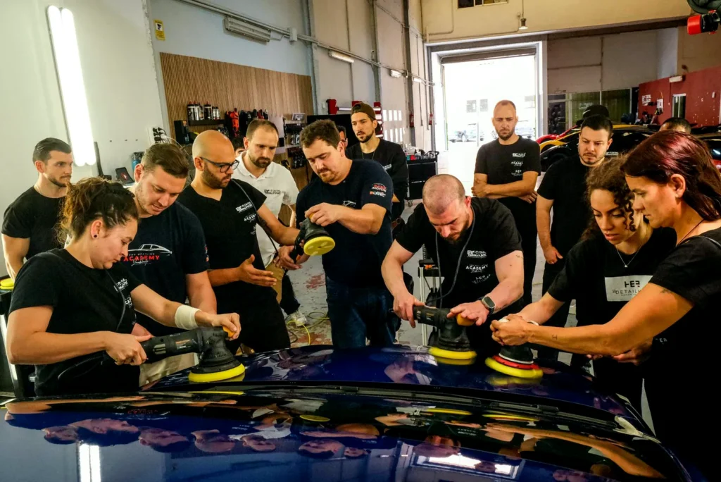 El Equipo 28 Una docena de alumnos puliendo a la vez el techo de un coche azul durante una formación de Detail Park