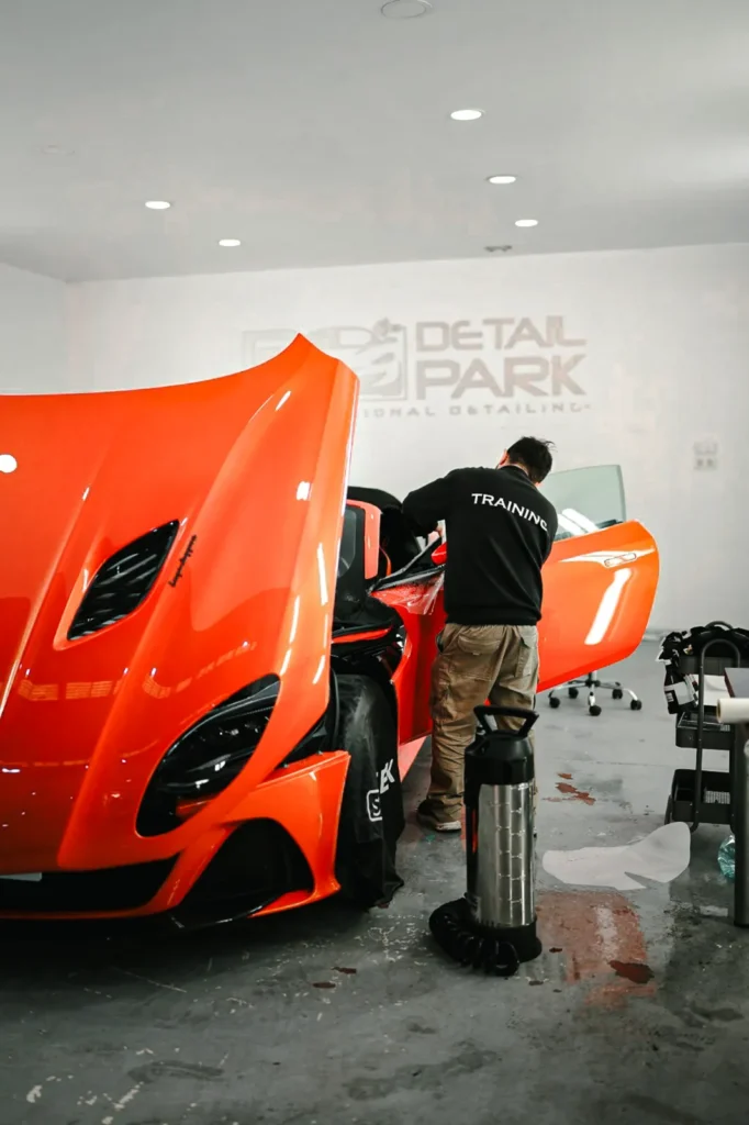 El Equipo 16 Instalador de espaldas colocando PPF en un Aston Martin DBS Superleggera naranja en el taller de Detail Park