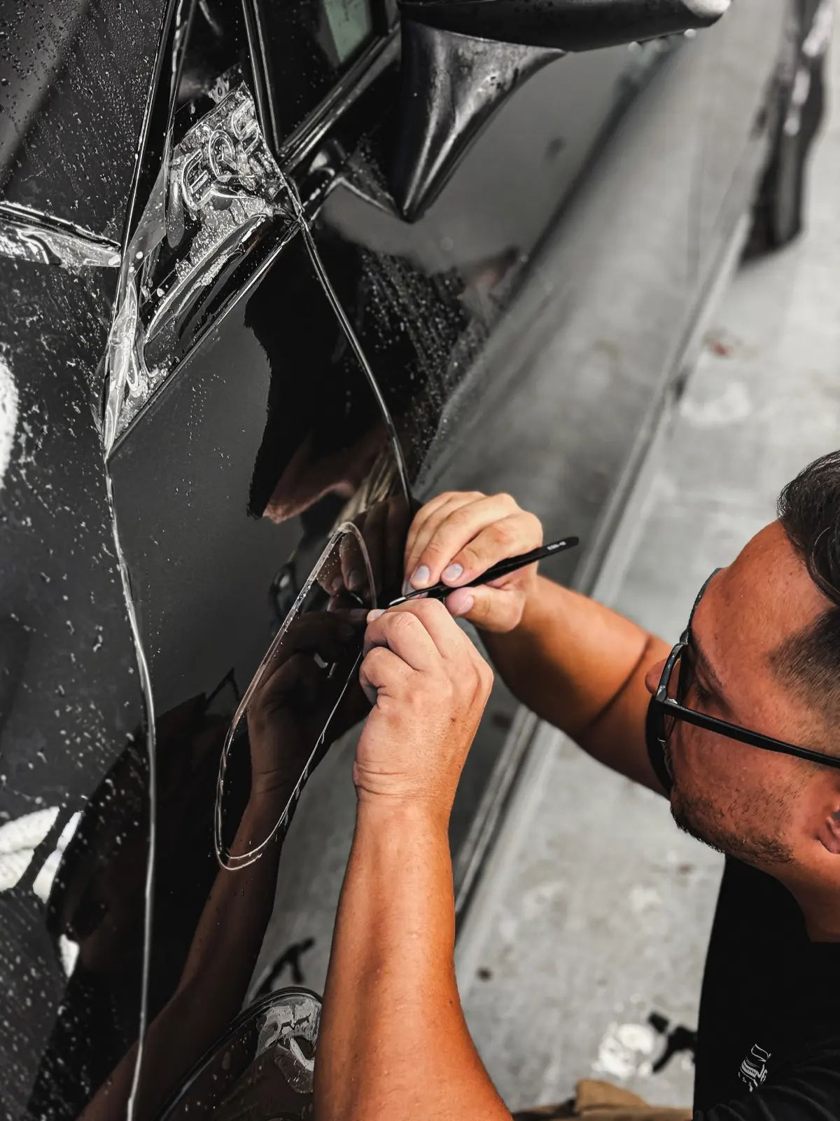 PPF Mercedes EQS SUV: protección integral con STEK DYNOshield 5 Instalador de Detail Park recortando el PPF STEK DYNOshield junto a la tapa de carga del Mercedes EQS