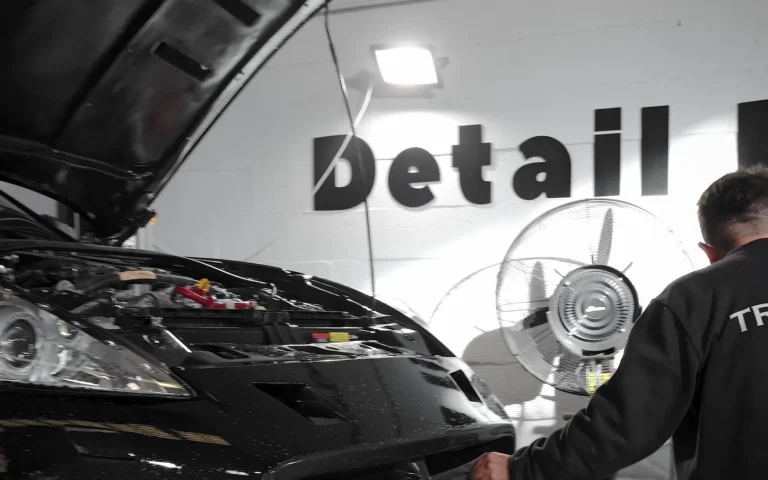 El Equipo 17 Nissan 370Z Nismo negro con el capó abierto durante la instalación de PPF frontal, con el rótulo de Detail Park en la pared