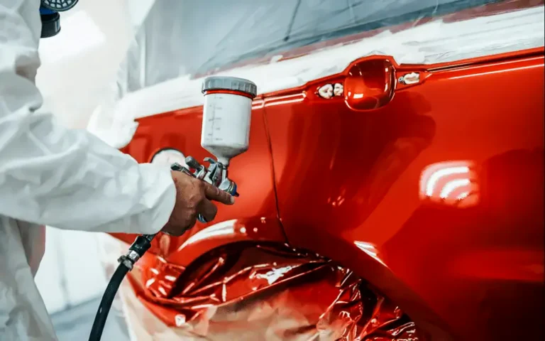 Pintor aplicando pintura roja con pistola en una aleta: cuánto cuesta pintar un coche
