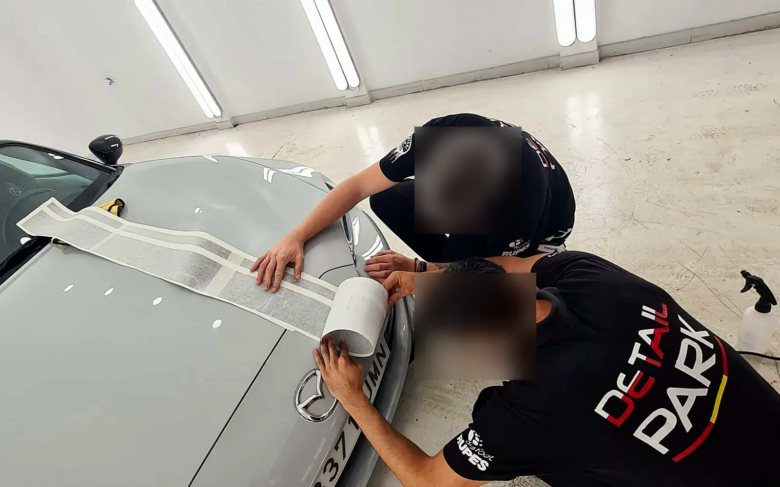 Vinilado Mazda MX-5: líneas en negro brillo y capó reparado 1 Vinilado Mazda MX-5: dos instaladores colocando las líneas de vinilo sobre el capó gris